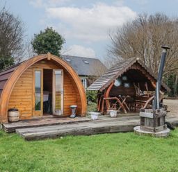 A wooden pod and covered seating area on a wooden deck with grass and trees at River View Pod near Muff County Donegal