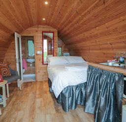 A wooden pod interior with a bed a small kitchenette two chairs a small table and a bathroom at River View Pod near Muff County Donegal
