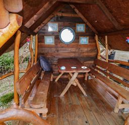 A small wooden cabin interior with a table and benches and framed pictures on the wall at River View Pod near Muff County Donegal