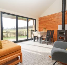A dining area with table and chairs next to a wood stove and large sliding glass doors at Beech Tree Cabin in Goodmanham near Market Weighton
