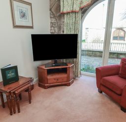 A corner of a room with a television on a wooden stand a red armchair and nested wooden tables at Aubretia Trail in Akeld near Wooler