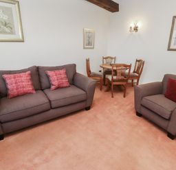 A living room with a sofa and armchair with red cushions and a wooden dining table with chairs at Aubretia Trail in Akeld near Wooler