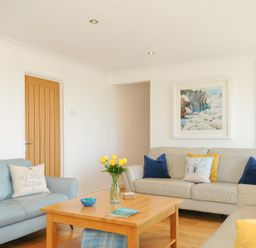 A living room with three sofas a wooden coffee table with flowers and a bowl and cushions on the sofas at Atlanta near Tintagel