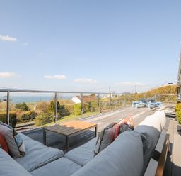 An outdoor terrace with a sofa and coffee table overlooking a garden and distant sea at Atlanta near Tintagel