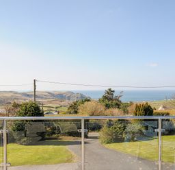 A view of a coastal landscape with grass and bushes seen from behind a glass balcony railing at Atlanta near Tintagel