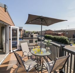 A balcony with a round glass table, four chairs, an umbrella, and drinks at Casa De Rhu in Evesham