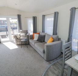 A living room with a gray sofa and armchair with cushions a small round table and dining table with chairs at Casa De Rhu in Evesham