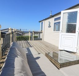 An outdoor deck area with a sofa and glass coffee table outside a beige building at 21 Bay View in Maenygroes near New Quay Ceredigion