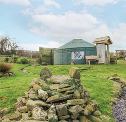 A garden with stone landscaping a small stream a circular tent and wooden bench at Blaidd Bach in Carmarthen