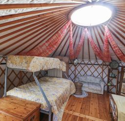 An interior of a yurt with a bunk bed mattress a sofa a wooden chest a small table and a standing mirror at Blaidd Bach in Carmarthen
