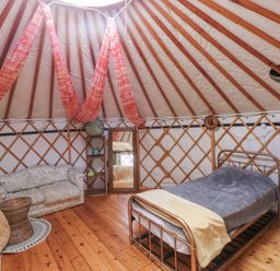 A room inside a yurt with a metal bed frame a couch a mirror and wooden floor at Blaidd Bach in Carmarthen