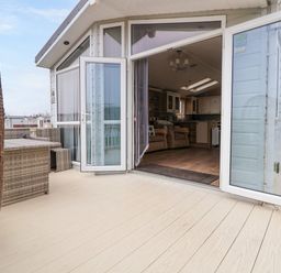 An outdoor patio with wicker furniture and a hanging chair next to an open door leading to a living area at Hazel Park Lodge HP4 in Rhyl