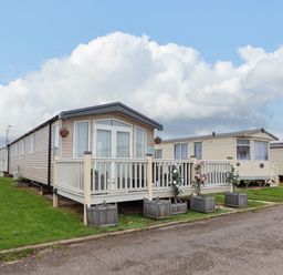 A row of beige mobile homes with porches and flower pots on a grassy area at Hazel Park 11 HP11 in Rhyl