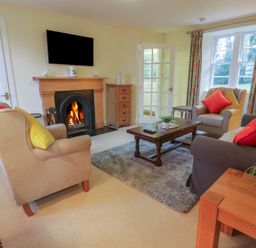 A living room with a fireplace a television armchairs a sofa coffee table and a window with curtains at Eagle Glen Cottage in Kettins near Coupar Angus
