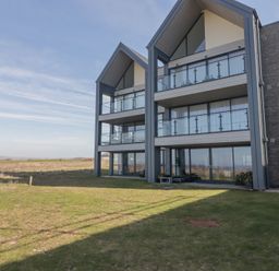 A modern multi-story building with balconies and large windows on a grassy area at The Links 40 An apartment with spectacular sea views Porthcawl