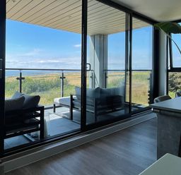 A balcony with outdoor seating overlooking a landscape seen through glass doors at The Links 40 in Porthcawl