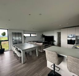 An open plan kitchen and living room with a dining table chairs sofas and large windows at The Links 40 An apartment with spectacular sea views in Porthcawl