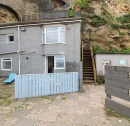 An outdoor patio area with two blue lounge chairs a stone building with windows and a door and a set of stairs leading up a rocky hillside at The Beach Apartment in South Shields