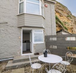An outdoor patio with a round table and four chairs with a bottle in an ice bucket on the table outside a grey stone building at The Beach Apartment in South Shields