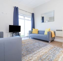 A living room with gray sofas yellow cushions a television on a stand a rug and a dining table at Atlantic Escape in Widemouth Bay