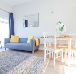 A living room with a gray sofa yellow pillows a wooden dining table with white chairs and flowers on it at Atlantic Escape in Widemouth Bay
