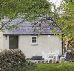 An outdoor area with white metal chairs and table near a stone wall and cottage at Cwt Mochyn in Llanberis