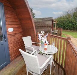 A wooden porch with two white chairs and a round table holding flowers and a bottle of wine at Chantelles in Holbeach