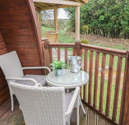 A small wooden balcony with two wicker chairs a round glass table with glasses and a plant at Charlottes Holbeach