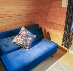 A blue sofa with two cushions next to a wooden wall and a door with patterned curtains at Charlottes in Holbeach