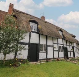 A traditional thatched cottage with white walls black timber framing and a garden with flowers at Church View in Welford-On-Avon