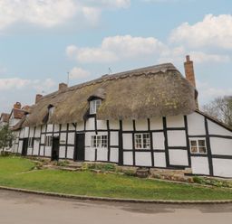A thatched roof cottage with white walls and black timber framing beside a road at Church View in Welford-On-Avon