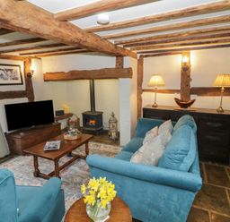 A living room with wooden beams a blue sofa two armchairs a wooden coffee table a fireplace and a television at Church View in Welford-On-Avon