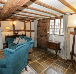 A living room with wooden beams stone floor and blue upholstered chairs at Church View in Welford-On-Avon