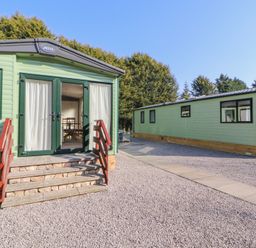 Two green mobile homes on gravel with wooden steps leading to a glass door at Lodge 1 in Silverdale