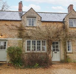 A stone cottage with multiple windows a vine climbing around the door and bushes in front at Little Lemhill Farm Cottage in Lechlade-On-Thames