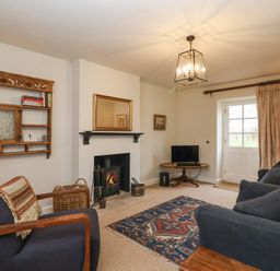 A living room with a fireplace, armchair, sofa, rug, wall shelf, small table with television, and a door with curtains at Little Lemhill Farm Cottage in Lechlade-On-Thames
