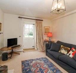A living room with a dark sofa and patterned rug near a door at Little Lemhill Farm Cottage in Lechlade-On-Thames
