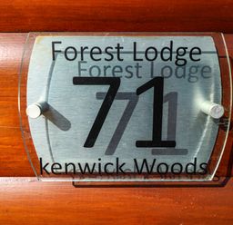 A wooden wall with a metal and glass house number sign showing 71 at Forest Lodge Kenwick Woods