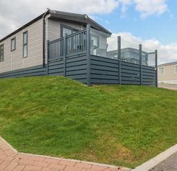 A modern mobile home with a fenced deck on a grassy slope at The Maples No 48 in Hewas Water near Sticker