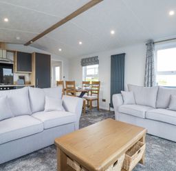 A living area with two sofas and a wooden coffee table adjacent to a dining table and kitchen at The Maples No 48 in Hewas Water near Sticker