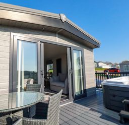 A patio with glass table and wicker chairs next to a hot tub outside a building with sliding glass doors at The Maples No 48 in Hewas Water near Sticker