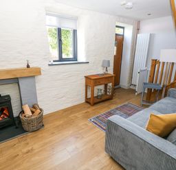 A living room with a wood burning stove basket of firewood wooden side table sofa and staircase at 3 The Barn in Haverfordwest