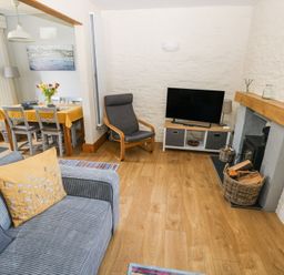 A living room with a gray sofa, armchair, television on a stand, dining table with a yellow tablecloth, and fireplace at 3 The Barn in Haverfordwest