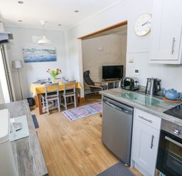 A kitchen and dining area with a yellow tablecloth on the table and a living room with a chair and television at 3 The Barn in Haverfordwest