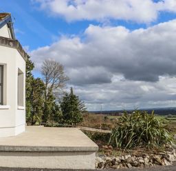 A concrete patio next to a white building with a garden and trees overlooking fields at Heatherbell House Ballyhoura near Buttevant