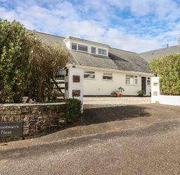 A white house with a grey roof and gravel driveway surrounded by bushes at Coastmans Nest in Mawgan Porth