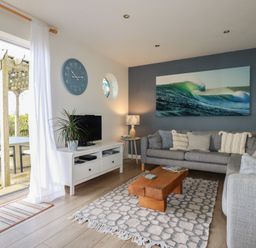 A living room with a wooden coffee table on a patterned rug and a gray sofa at Coastmans Nest in Mawgan Porth