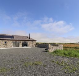 A stone building with solar panels and gravel area at West Burton Hemmel in Bamburgh