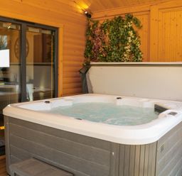 A wooden room with a hot tub and a sliding glass door showing a kitchen at Alpaca Lodge in Barkston