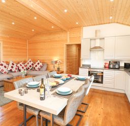 An open plan kitchen and living room with a dining table set for six and a grey sofa with red polka dot cushions at Alpaca Lodge in Barkston